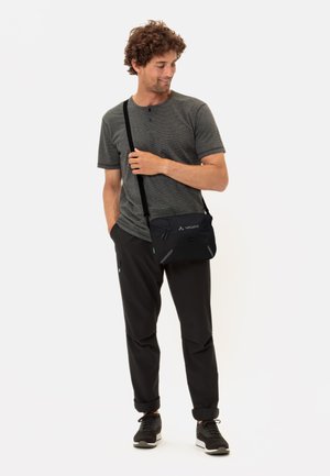 Sac à bandoulière noir avec plusieurs poches, sangle réglable, fermetures à glissière et logo. Tissu léger avec une texture lisse.