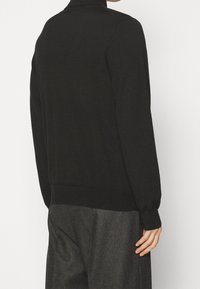 Czarny dzianinowy sweter z wysokim kołnierzem, ściągaczowymi mankietami i dołem. Tył ma gładką fakturę i dopasowany krój.