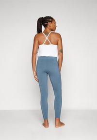 Weißes Cropped Top mit überkreuzten Trägern, kombiniert mit blauen, eng anliegenden Leggings. Glatte Textur und dehnbares Design, geeignet für Sportbekleidung.