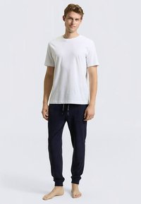 Weißes Kurzarm-T-Shirt kombiniert mit marineblauen Jogginghosen mit elastischem Bund und Kordelzug, präsentiert von einem barfuß stehenden Modell.