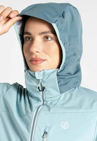 Hellblauer Kapuzenjacke mit hohem Kragen, Reißverschluss und kontrastierender Innenseite. Auffälliges Logo im Brustbereich. Glatte Textur.