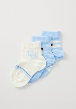 Set aus drei Socken: eine weiße mit blauen Akzenten und "TH"-Logo, zwei hellblaue, eine mit Streifen und roten Akzenten. Material aus Baumwollmischung.