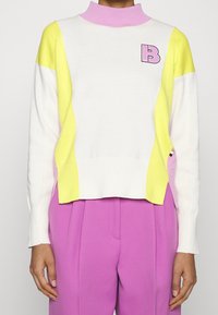 Pull color-block en blanc, jaune et rose. Design à col montant côtelé avec un détail logo. Texture douce, coupe légèrement ample.