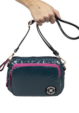 Bolso acolchado en verde azulado con una cremallera rosa y detalles en negro. Cuenta con un bolsillo frontal, correas ajustables negras y un detalle de logo circular.