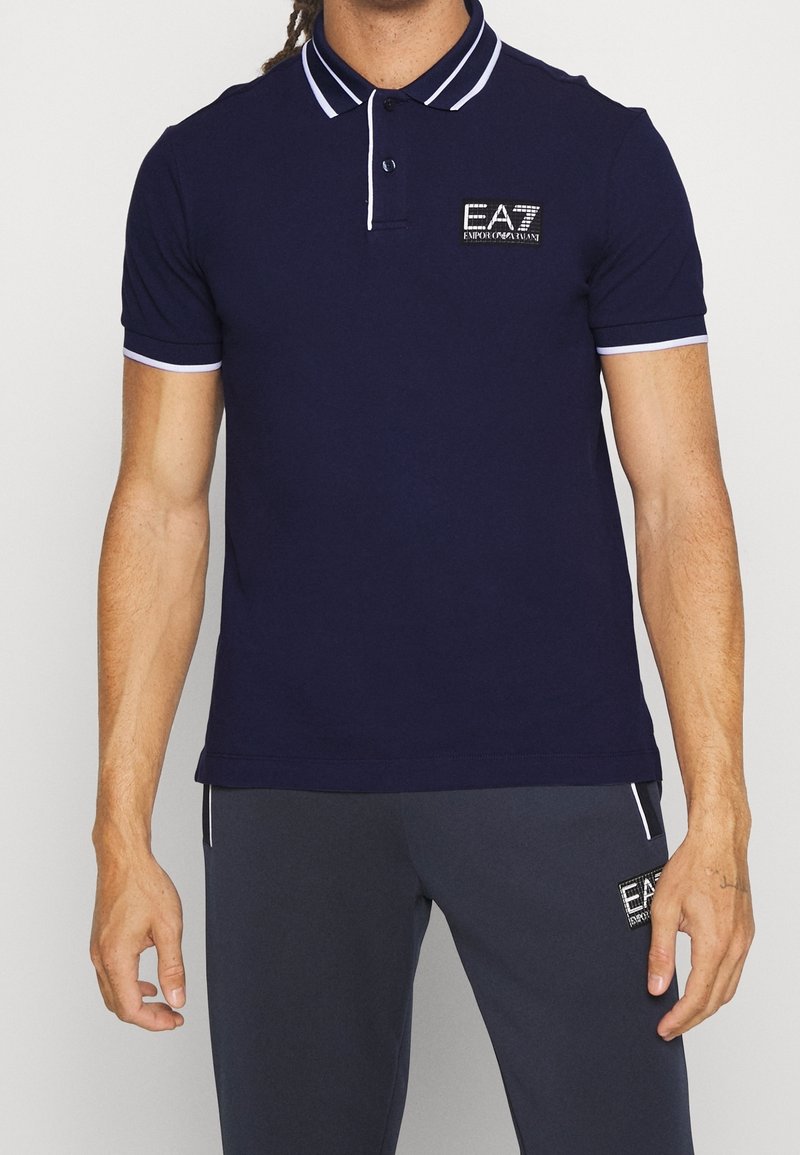 Marinblå polo skjorta med vit och ljusblå kant, med en vävd EA7 logotyp på bröstet. Tillverkad av slät, andningsbar tyg.