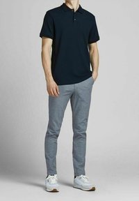 Granatowa, prążkowana koszulka polo z krótkim rękawem, w zestawie z jasnoszarymi, dopasowanymi spodniami oraz białymi butami sportowymi z brązowymi podeszwami.