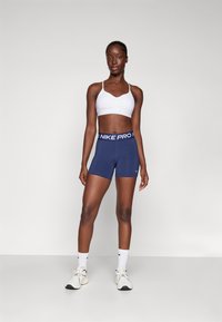 Nike Pro sports-bh i hvid, parret med marineblå Nike Pro shorts med elastisk talje. Modellen har hvidt fodtøj og sokker på.