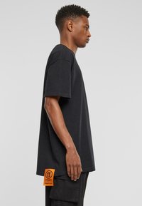 Black oversized t-shirt made of cotton with short sleeves and an orange tag featuring "ff" and "240gsm" on the left side.