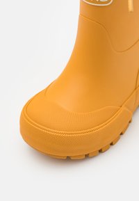Botte en caoutchouc jaune avec surface texturée, bout arrondi et semelle extérieure durable dotée de profondeurs pour une meilleure adhérence.
