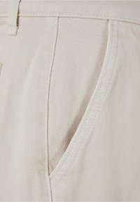 Pantalones de algodón color beige claro con una tela texturizada, bolsillo lateral curvado y costuras precisas a lo largo de las costuras para mayor durabilidad.