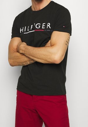 T-shirt en coton noir avec le logo blanc "HILFIGER", des lignes d'accent rouge et bleu, des manches courtes et un col rond classique.