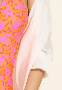 Zbliżenie dwóch torsów obok siebie, jeden w różowo-pomarańczowej sukience w kwiaty, a drugi w białej koszuli o teksturze z podwiniętymi rękawami.