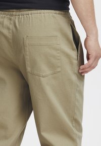 Khaki pants with a relaxed fit, featuring a back pocket, side pockets, and an elastic waistband. Made from cotton blend fabric.