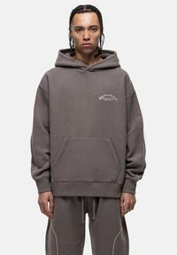 Felpa grigia con cappuccio, tasca frontale e dettagli di cucitura bianca, caratterizzata da del testo stampato in piccolo sul petto.