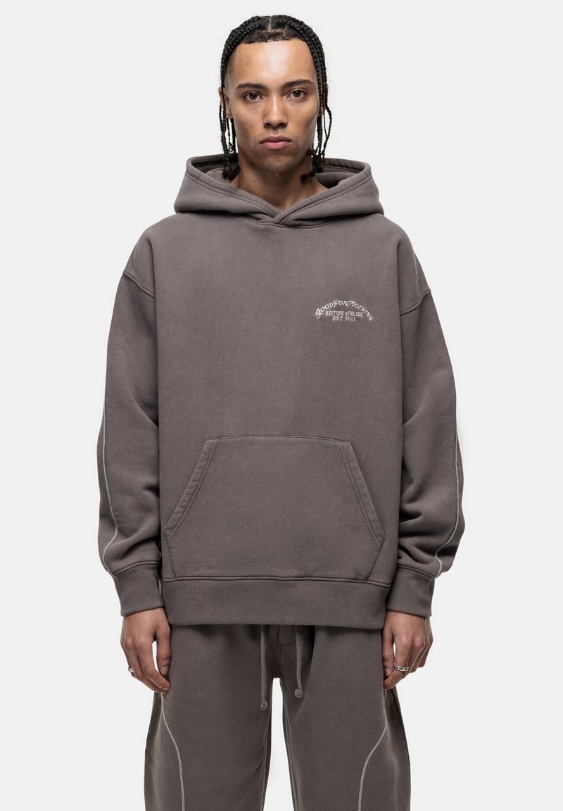 Felpa grigia con cappuccio, tasca frontale e dettagli di cucitura bianca, caratterizzata da del testo stampato in piccolo sul petto.