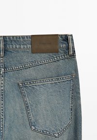 Jeans in denim blu sbiadito con un'etichetta in pelle marrone sulla vita e un semplice design della tasca posteriore.