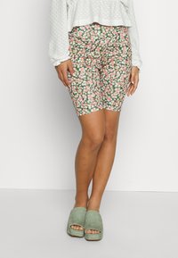 Calças de ciclismo com padrão floral em rosa, branco e verde, com um design ajustado, combinadas com sapatos de camurça verde de salto plataforma.