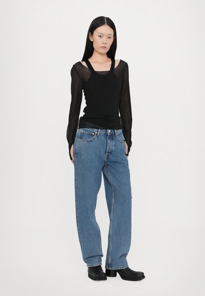 Μαύρο μπλουζάκι μακρυμάνικο με διάφανες μανσέτες, συνδυασμένο με χαλαρά μπλε τζιν και μαύρες χοντρές μπότες με τακούνι. Απλός και casual σχεδιασμός.