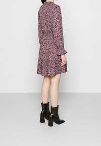 Röd blommönstrad klänning med lång ärm, volangkant och smockad midja, kombinerad med svarta ankle boots med blockklack.