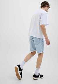 Tricou alb din bumbac, pantaloni scurți din denim albastru deschis cu marginile răsucite, adidași negri cu accente albe și șosete albe. O ținută simplă și lejeră.