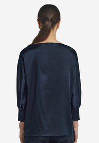 Granatowa satynowa bluzka z szerokim dekoltem, długimi bufkami i gładką fakturą. Z tyłu znajduje się subtelny szew biegnący wzdłuż środka.