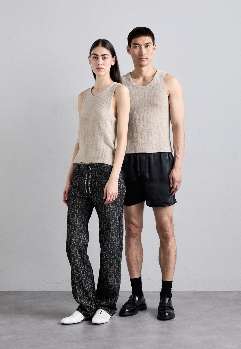 Beige strukturierte Tanktops, gemusterte schwarze Hosen mit Kordelzug, schwarze Shorts und Schuhwerk: weiße Slipper und schwarze Mokassins.