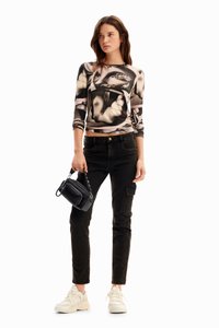 Top a maniche lunghe aderente con un design grafico in bianco e nero, abbinato a jeans neri, una piccola borsa nera e sneaker beige.