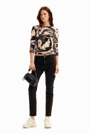 Top a maniche lunghe aderente con un design grafico in bianco e nero, abbinato a jeans neri, una piccola borsa nera e sneaker beige.