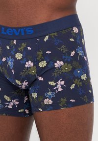 Levi's blommiga kalsonger har en marinblå grund med en mängd rosa, blå och gröna blommor. Midjan är enfärgad marinblå med en blå logotyp.