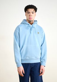 Light blue hooded sweatshirt made of cotton, featuring a front pocket, adjustable drawstrings, and a small logo patch on the chest.