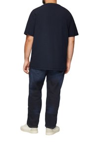 Marineblauwe katoenen T-shirt met korte mouwen en een ronde hals, gecombineerd met donkerdenim jeans en lichtgekleurde sneakers.