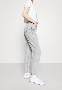 Grå högmidjade jeans med lös passform, med en klassisk femficksdesign, kombinerat med vita högstövlar.