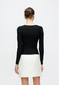 Μαύρη μακρυμάνικη μπλούζα με υφασμένο μοτίβο, εφαρμοστή σχεδίαση και στρογγυλη λαιμόκοψη, συνδυασμένη με λευκή υφασμένη φούστα.