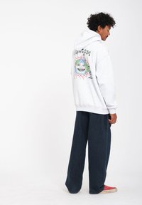 Gray hooded sweatshirt with a colorful graphic featuring a smiling earth and sun design on the back, paired with dark wide-leg pants.