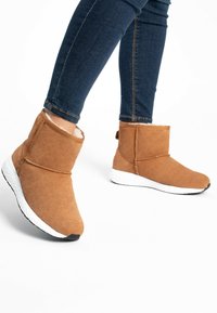 Brune ankelstøvler lavet af blødt materiale med en hvid tekstureret sål, der har et foldet design og fuzzy foring, velegnet til afslappet brug.