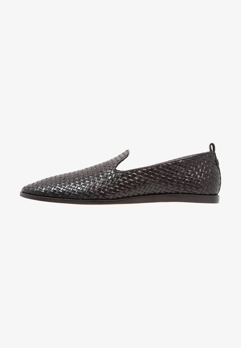 Chaussure noire en cuir tressé à enfiler, bout pointu, semelle plate basse et petite languette au talon à l'arrière.