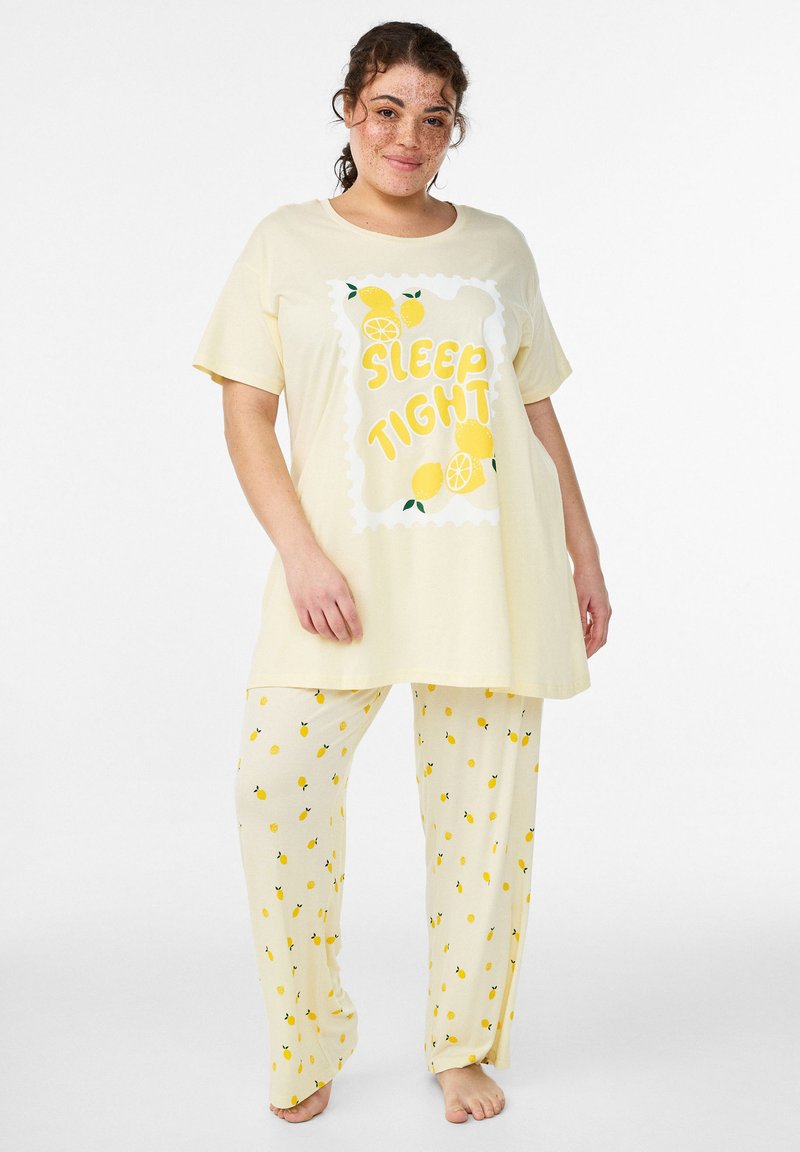 Ensemble de pyjama jaune clair comprenant un haut à manches courtes avec le texte "DORS BIEN" et des illustrations de citrons, accompagné d'un pantalon long orné de motifs de citrons.
