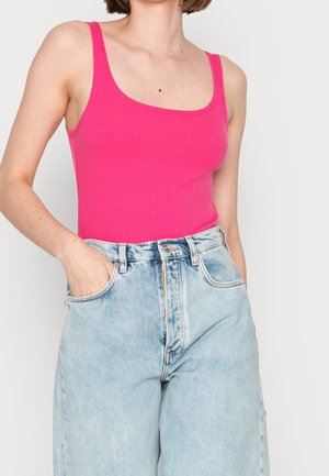 Fuksjowy prążkowany top na ramiączkach z szerokimi paskami i kwadratowym dekoltem, w połączeniu z jasnoniebieskimi dżinsami z wysokim stanem.