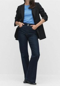 Modrá košile, černý blazer a tmavé džíny s rozšířenými nohavicemi. Džíny mají vysoký pas a přední zapínání na knoflík. Hladká textura látky.