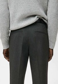 Maglione grigio a coste sopra pantaloni di lana grigio scuro, caratterizzati da due tasche posteriori e un design a vita piatta, con una texture liscia e una vestibilità sartoriale.