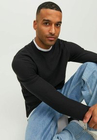 Maglietta nera a maniche lunghe in tessuto testurizzato con collo a giro, abbinata a jeans in denim blu chiaro, con cuciture visibili e una vestibilità casual.