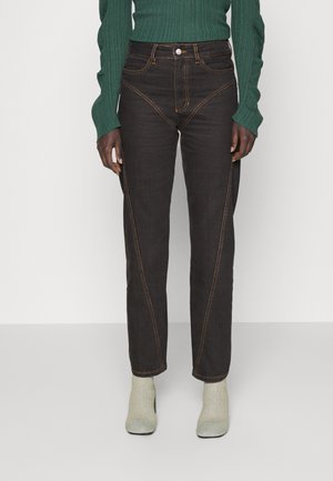 Σκοτεινά τζιν παντελόνια με αντίθετη πορτοκαλί ραφή, ψηλή μέση και σχεδίαση ευθείας γραμμής. Φορεμένα με ένα πράσινο ριγέ πουλόβερ και ανοιχτόχρωμες κάλτσες.