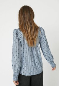 Blue and white striped shirt featuring puff sleeves, smocked cuffs, and a pattern of dark circles throughout the fabric.
