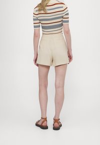 Beiga shorts med skräddarsydd passform, med sidofickor, en mjuk textur och en bakre dragkedja, i kombination med bruna sandaler med remmar.