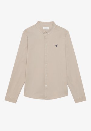 Beige knap-up skjorte med lange ærmer, en klassisk krave, og et lille marineblåt fuglelogo broderet på brystet. Blød stoftekstur.