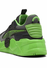 Grå sneakers med en texturerad yta, gröna detaljer, tjock sula och en framträdande etikett som hänger från snörningssystemet.