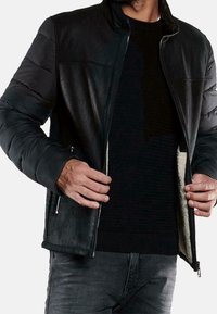 Musta nahkatakki, jossa on pehmustetut hihnat, vetoketjusuljenta ja pehmeä sisävuori. Päällä musta teksturoitu villapaita ja harmaat farkut.