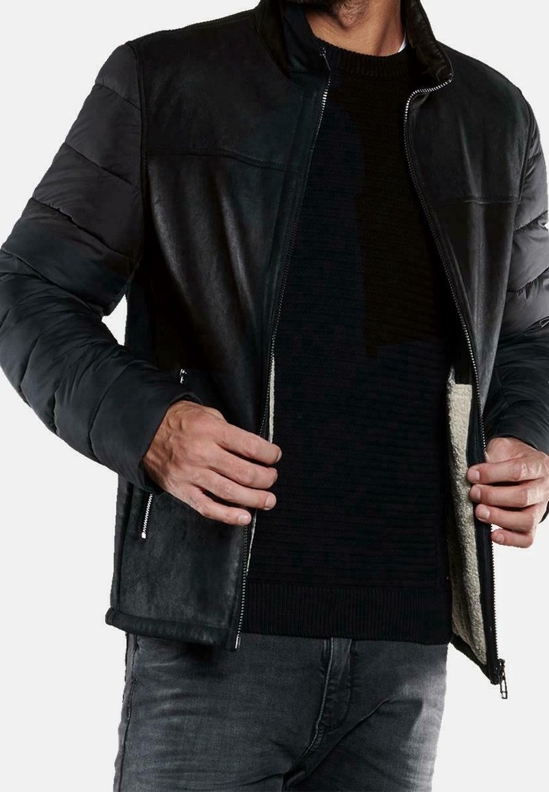 Musta nahkatakki, jossa on pehmustetut hihnat, vetoketjusuljenta ja pehmeä sisävuori. Päällä musta teksturoitu villapaita ja harmaat farkut.