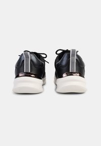 Chaussures de sport noires avec une tige en cuir lisse, des accents en tissu, des détails réfléchissants et une semelle texturée blanche. Lacets et tirants inclus.