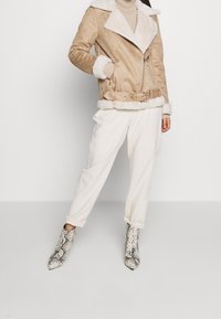 Beige mockajacka med fuskpäls på krage och ärmslut, bältad i midjan. Kombinerad med krämfärgade byxor och spetsiga ankelboots med ormmönster.